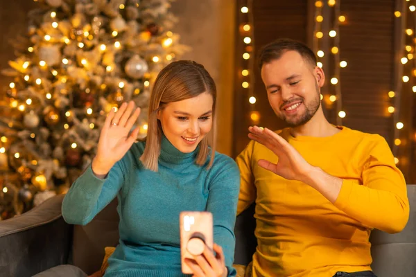 Jeune couple amoureux célébrant Noël à la maison. Jeune homme et sa jolie petite amie dans un intérieur de maison avec un arbre de Noël. — Photo