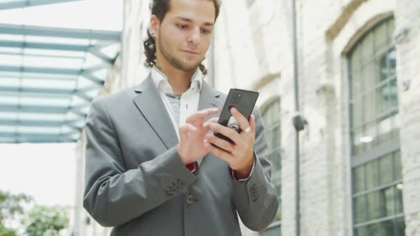 Mladý úspěšný podnikatel pracuje venku pomocí chytrého telefonu. Muž v neformálním oblečení. Práce na volné noze a na dálku. — Stock video