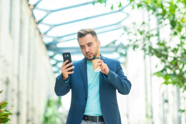Genç ve başarılı bir iş adamı akıllı telefon kullanarak dışarıda çalışıyor. Sıradan giysili bir adam. İş, serbest meslek ve uzak çalışma.