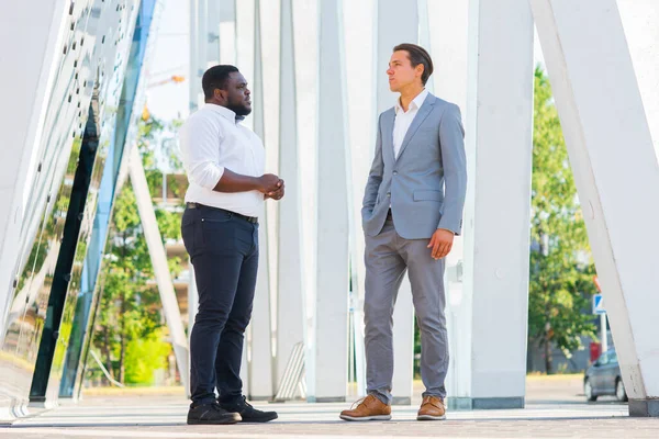 Der afroamerikanische Geschäftsmann und sein Kollege vor einem modernen Bürogebäude. Finanzinvestoren reden im Freien. Bank- und Geschäftskonzept. — Stockfoto