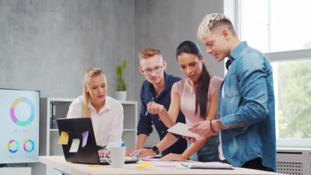 Une équipe de jeunes startupers travaille à la table du bureau, discutant de la stratégie et du plan de développement de l'entreprise. Concept d'entreprise, d'innovation, de réflexion et de travail d'équipe. — Video