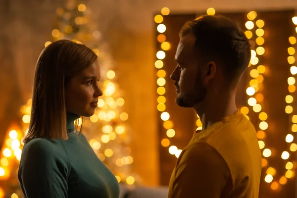 Las siluetas de un hombre joven y atractiva chica en el interior de una casa con luces y un árbol de Navidad en el fondo. Joven pareja amorosa celebrando la Navidad. — Foto de Stock