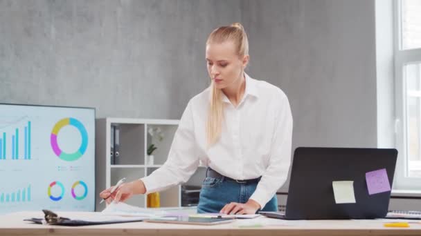 Lugar de trabajo del trabajador independiente o de una estudiante en la oficina del hogar. Mujer joven trabaja usando la computadora y otros dispositivos. Concepto de trabajo remoto. — Vídeos de Stock