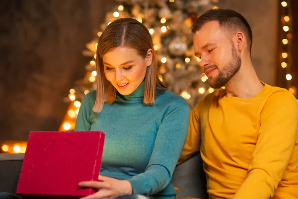 Jeune couple amoureux célébrant Noël à la maison. Jeune homme et sa jolie petite amie dans un intérieur de maison avec un arbre de Noël. — Photo