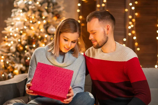 Jeune couple amoureux célébrant Noël à la maison. Jeune homme et sa jolie petite amie dans un intérieur de maison avec un arbre de Noël. — Photo