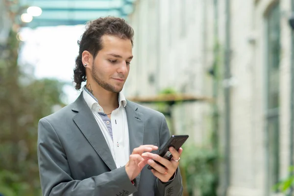 Ein junger erfolgreicher Geschäftsmann arbeitet im Freien mit dem Smartphone. Mann in Freizeitkleidung. Unternehmen, Freiberufler und Fernarbeit. — Stockfoto