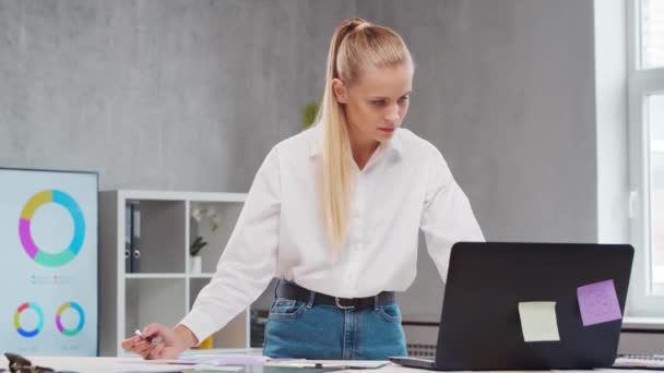 Lugar de trabajo del trabajador independiente o de una estudiante en la oficina del hogar. Mujer joven trabaja usando la computadora y otros dispositivos. Concepto de trabajo remoto. — Vídeos de Stock