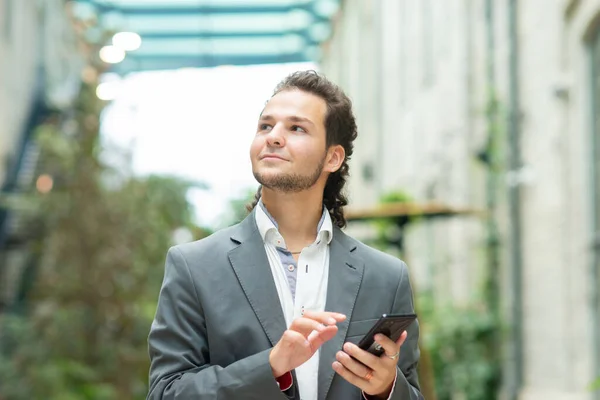 Ένας νεαρός επιτυχημένος επιχειρηματίας εργάζεται σε εξωτερικούς χώρους χρησιμοποιώντας smartphone. Ένας άντρας με ένα απλό ντύσιμο. Επαγγελματική, ανεξάρτητη και εξ αποστάσεως εργασία. — Φωτογραφία Αρχείου