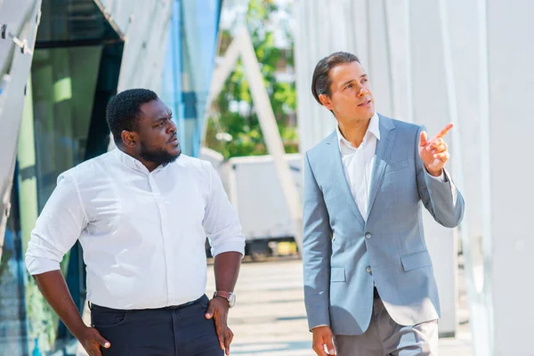 Uomo d'affari afro-americano e il suo collega di fronte a un moderno edificio per uffici. Gli investitori finanziari stanno parlando all'aperto. Concetto bancario e aziendale. — Foto Stock