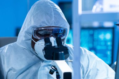 Koruyucu kıyafetli Afrikalı-Amerikalı doktor modern bir laboratuvarda bilimsel deneyler yapıyor ve aşı geliştiriyor. Laboratuvar asistanı iş yerinde. Bilim ve tıp kavramı.
