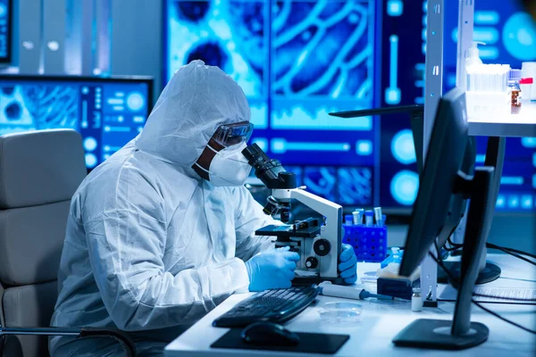 El médico afroamericano en traje protector está haciendo experimentos científicos y desarrollando vacunas en un laboratorio moderno. Laboratorio asistente de trabajo. El concepto de ciencia y medicina. — Foto de Stock