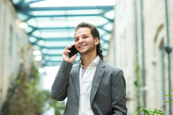 En ung framgångsrik affärsman arbetar utomhus med hjälp av smartphone. En man i vardagskläder. Affärer, frilans och distansarbete. — Stockfoto