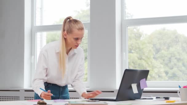 Lugar de trabajo del trabajador independiente o de una estudiante en la oficina del hogar. Mujer joven trabaja usando la computadora y otros dispositivos. Concepto de trabajo remoto. — Vídeos de Stock