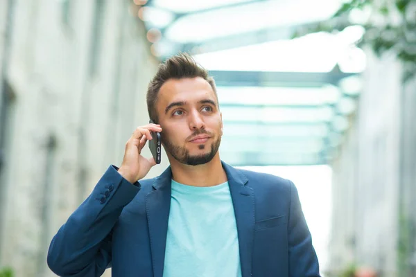 Un joven empresario exitoso está trabajando al aire libre con un teléfono inteligente. Un hombre con ropa casual. Negocios, freelance y trabajo remoto. —  Fotos de Stock