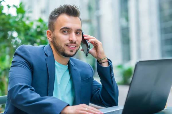 Jonge succesvolle Kaukasische zakenman werkt in een outdoor cafe met behulp van een computer. Bedrijven, freelance en werk op afstand. — Stockfoto