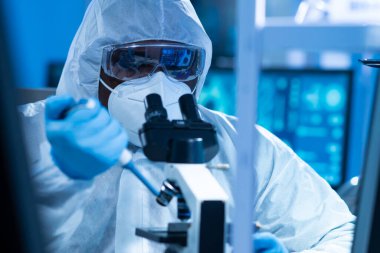 Koruyucu kıyafetli Afrikalı-Amerikalı doktor modern bir laboratuvarda bilimsel deneyler yapıyor ve aşı geliştiriyor. Laboratuvar asistanı iş yerinde. Bilim ve tıp kavramı.