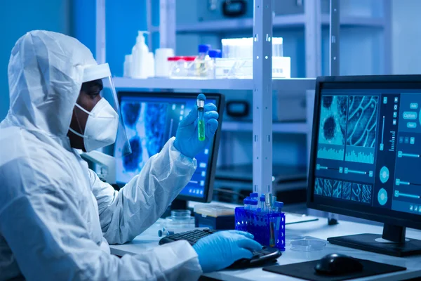 El médico afroamericano en traje protector está haciendo experimentos científicos y desarrollando vacunas en un laboratorio moderno. Laboratorio asistente de trabajo. El concepto de ciencia y medicina. —  Fotos de Stock