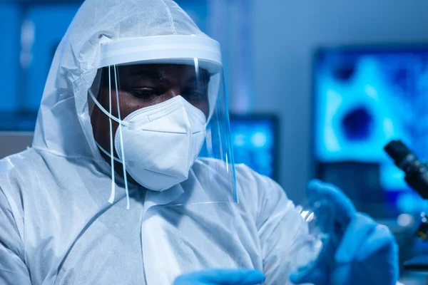 El médico afroamericano en traje protector está haciendo experimentos científicos y desarrollando vacunas en un laboratorio moderno. Laboratorio asistente de trabajo. El concepto de ciencia y medicina. — Foto de Stock