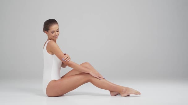 Young, beautiful, fit and natural blond woman in white swimsuit applying moisturizing cream. Massage, skin care, cellulite removal, sport and weight loss. — Stock Video