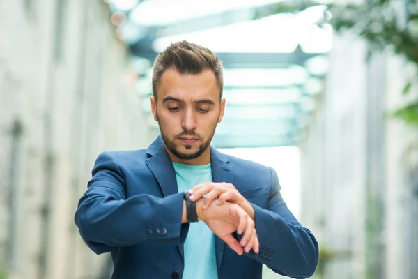 A young successful businessman is working outdoor using smartwatch. Man in a casual wear. Business, freelance and remote work. — Stock Photo, Image