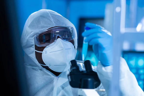 Afroamerykanin w kombinezonie ochronnym robi eksperymenty naukowe i opracowuje szczepionkę w nowoczesnym laboratorium. Asystent laboratoryjny w pracy. Koncepcja nauki i medycyny. — Zdjęcie stockowe