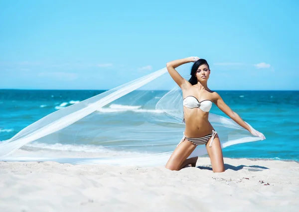 Женщина позирует с дующим шелком на пляже — стоковое фото