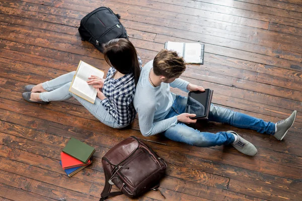 Mädchen lesen ein Buch und Junge benutzen ein Tablet — Stockfoto