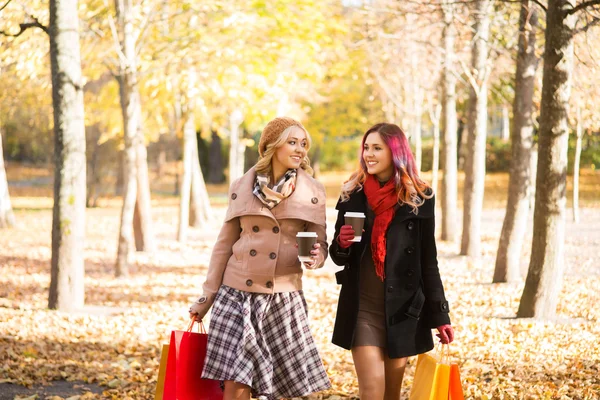Дві красиві жінки мають розслаблюючу розмову з кавою після покупки ходьби в осінньому парку — стокове фото