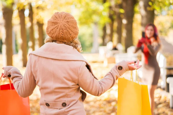 Two beautiful young women taking photographs in the autumn with shopping bags — Stock Photo, Image