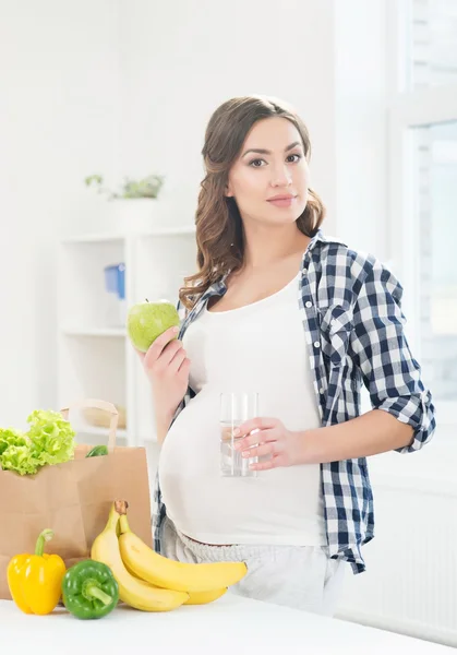 Beautiful pregnant woman in the kitchen with shopping bag and apple — Stock Photo, Image