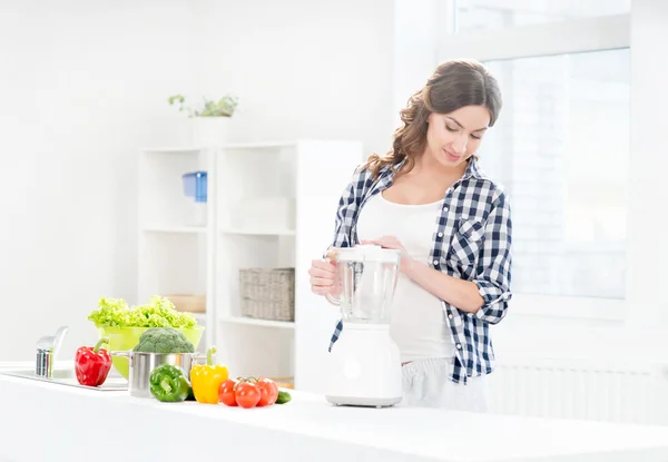 Schöne schwangere lächelnde Frau, die mit einem Mixer kocht — Stockfoto