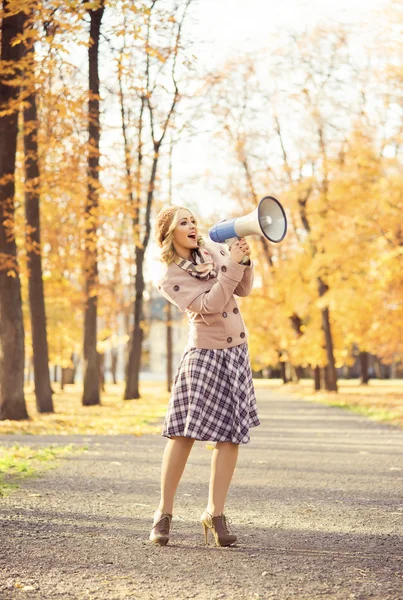 Woman yelling with loudspeaker in the autumn park — Stock Photo, Image