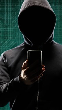İkili kodlu dijital arkaplanda akıllı telefon aygıtı olan tehlikeli bir hacker. Maske ve kapüşonlu karanlık yüz. Veri hırsızlığı, internet saldırısı, darknet dolandırıcılığı, sanal gerçeklik ve siber güvenlik kavramı.
