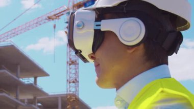 İnşaat alanının önünde duran profesyonel müteahhit. Kasklı ve yelekli ustabaşı. Ofis binası ve vinç arka planı. İş, gayrimenkul ve yatırım kavramları.