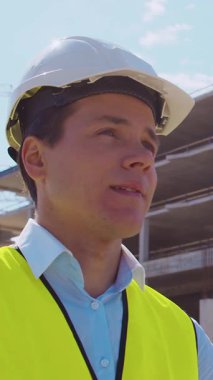 İnşaat alanının önünde duran profesyonel müteahhit. Kasklı ve yelekli ustabaşı. Ofis binası ve vinç arka planı. İş, gayrimenkul ve yatırım kavramları.