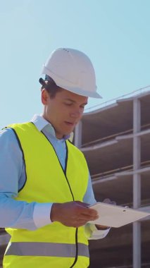 İnşaat alanının önünde duran profesyonel müteahhit. Kasklı ve yelekli ustabaşı. Ofis binası ve vinç arka planı. İş, gayrimenkul ve yatırım kavramları.