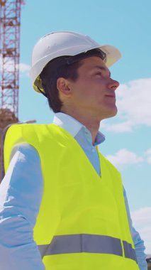 İnşaat alanının önünde duran profesyonel müteahhit. Kasklı ve yelekli ustabaşı. Ofis binası ve vinç arka planı. İş, gayrimenkul ve yatırım kavramları.