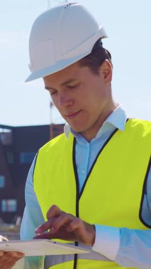 İnşaat alanının önünde duran profesyonel müteahhit. Kasklı ve yelekli ustabaşı. Ofis binası ve vinç arka planı. İş, gayrimenkul ve yatırım kavramları.