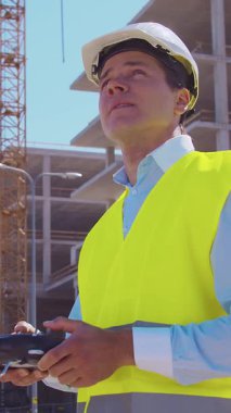 İnşaat alanının önünde duran profesyonel müteahhit. Kasklı ve yelekli ustabaşı. Ofis binası ve vinç arka planı. İş, gayrimenkul ve yatırım kavramları.