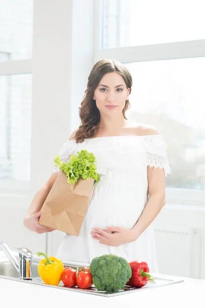 Pregnant woman with shopping bag in kitchen. — Stock Photo, Image