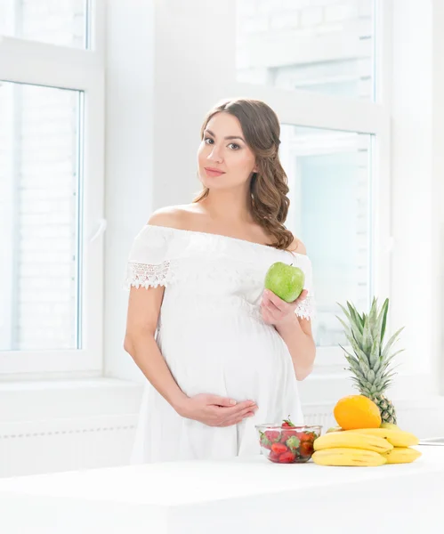 Donna incinta in cucina mangiare frutta — Foto Stock