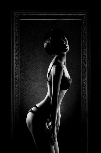 Svartvitt foto av ung sexig kvinna i erotiska underkläder stående i ramen — Stockfoto