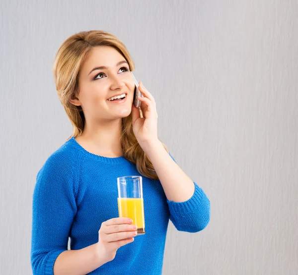 Chica joven bebiendo jugo de naranja y hablando por teléfono —  Fotos de Stock