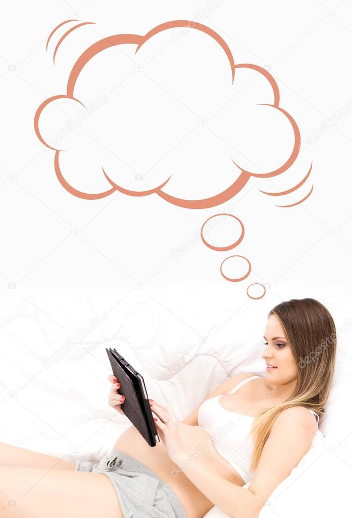 A young and pregnant woman holding a tablet computer in the bed 