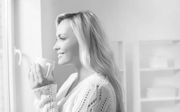 Young and beautiful woman drinking coffee and looking it to the window — Stock Photo, Image