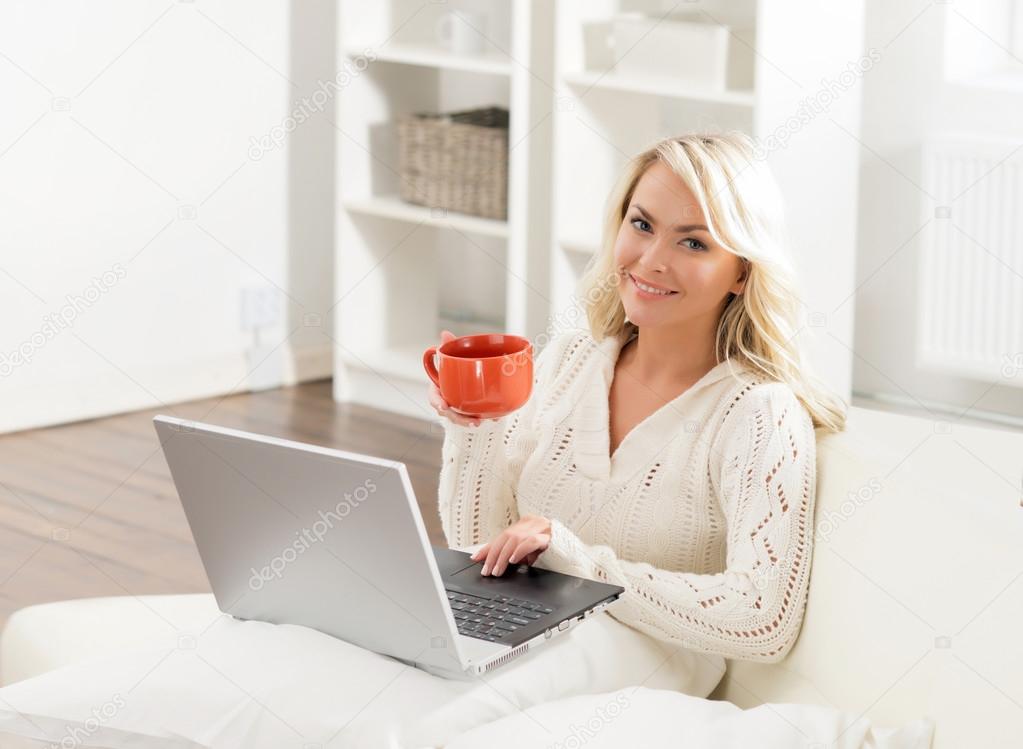 Beautiful woman using laptop and having a cup of coffee in the morning