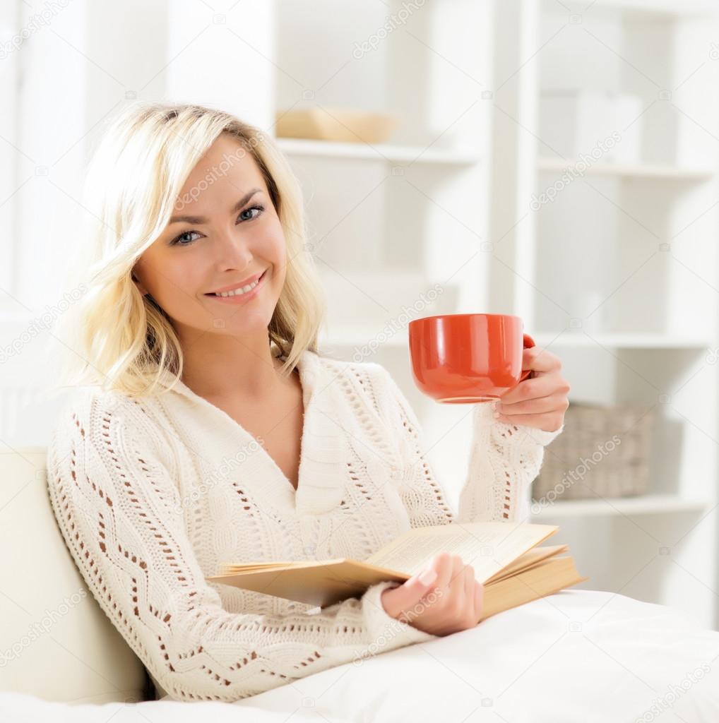 Beautiful smiling happy woman reading a book and having a cup of coffee