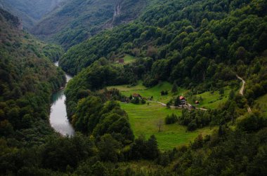 Üzerinde bir evin bulunduğu ve yakınlarda bir nehrin aktığı bir açıklığı olan ağaçlandırılmış dağlar.