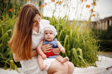 Yürümeye başlayan çocuk annesinin dizinin üstüne oturuyor 