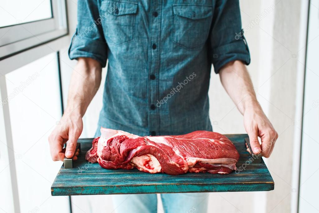 Man`s hands holding rustic tray with raw beef meet